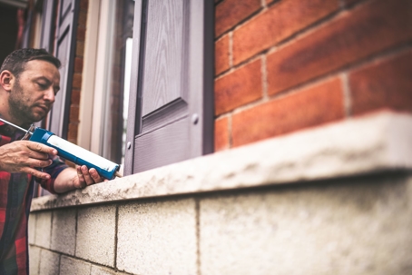Man filling windows with caulking.